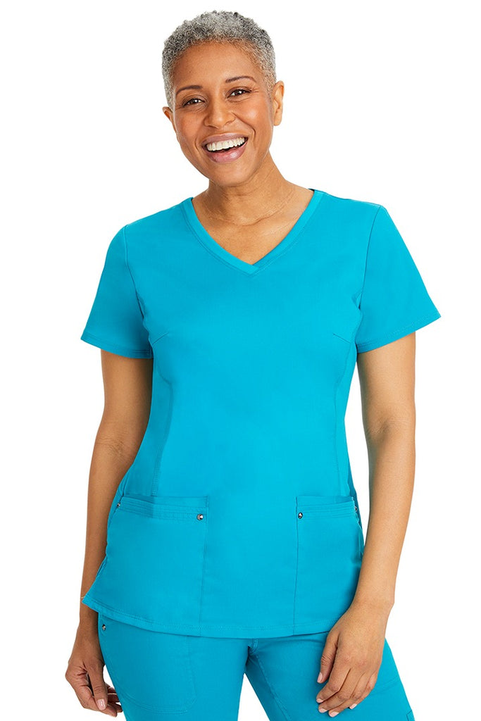 A young LPN wearing a Purple Label Women's Juliet Yoga Scrub Top in Teal featuring 2 front patch pockets.