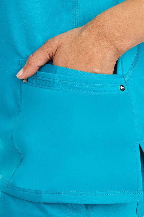 A young woman wearing a Women's Juliet Yoga Scrub Top from Purple Label by Healing Hands in Teal  featuring side slits for additional range of motion.