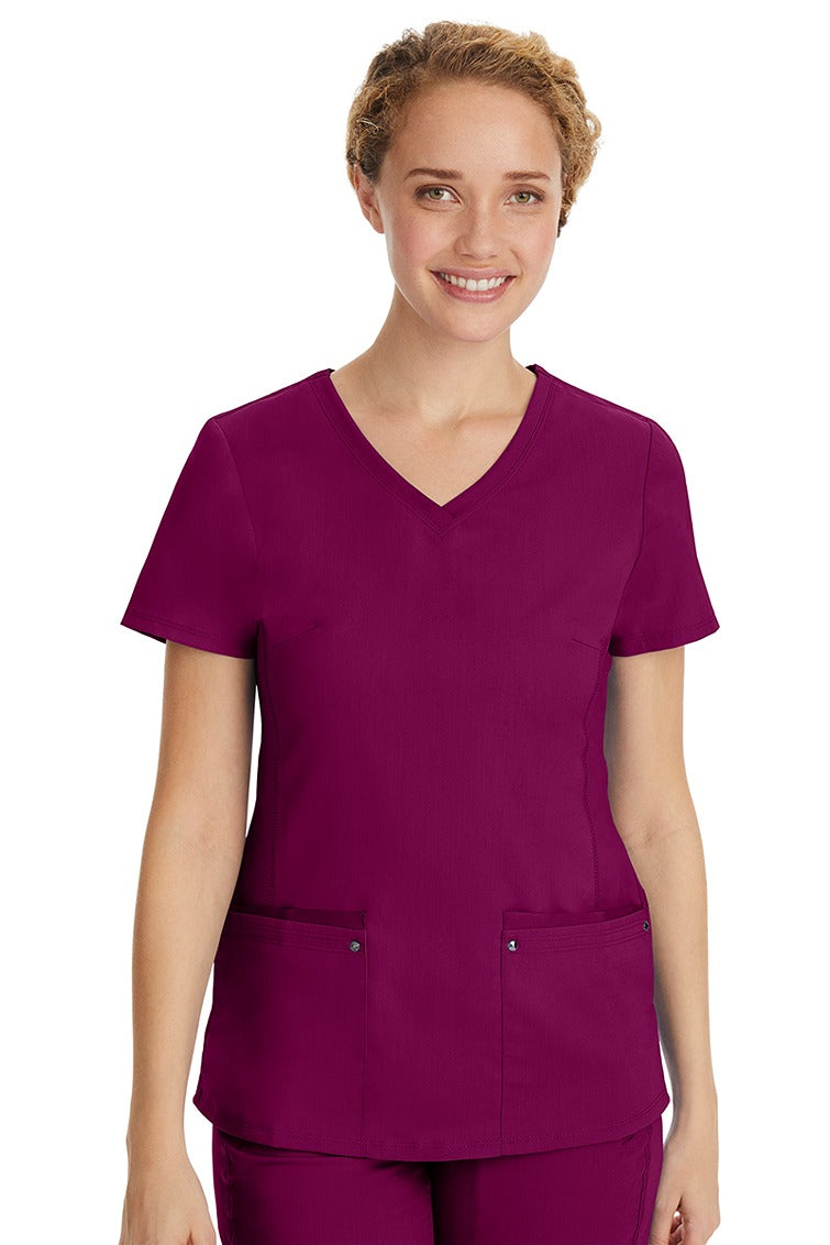 A young LPN wearing a Purple Label Women's Juliet Yoga Scrub Top in Wine featuring 2 front patch pockets.