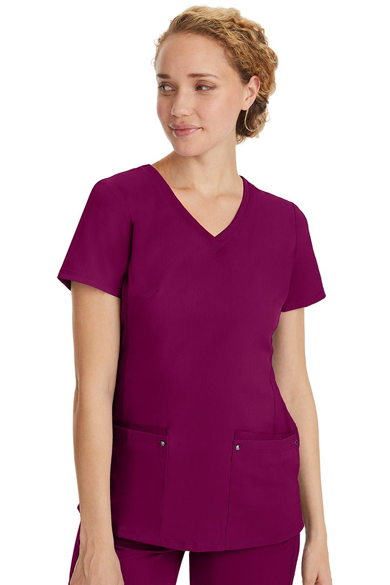 A female healthcare professional wearing a Women's Juliet Yoga Scrub Top from Purple Label in Wine featuring a side stretch panels.