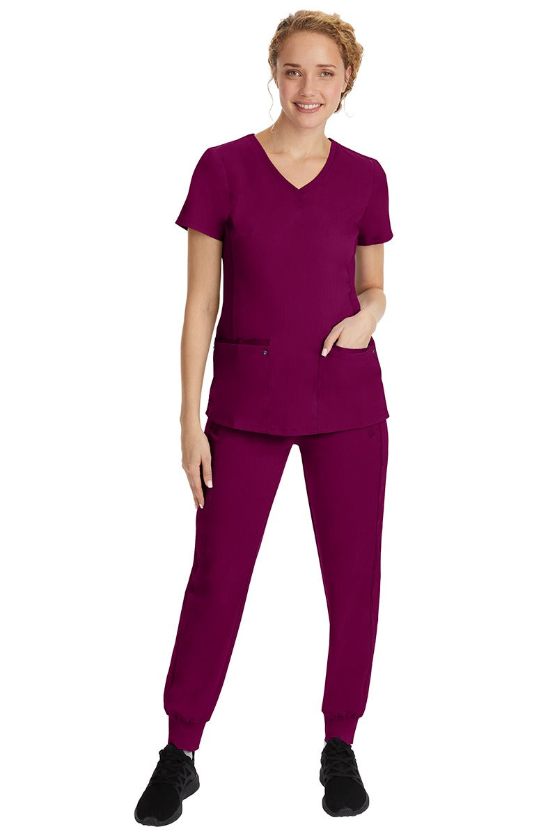 A young female nurse wearing a Purple Label Women's Juliet Yoga Scrub Top by Healing Hands in Wine featuring a v-neckline.