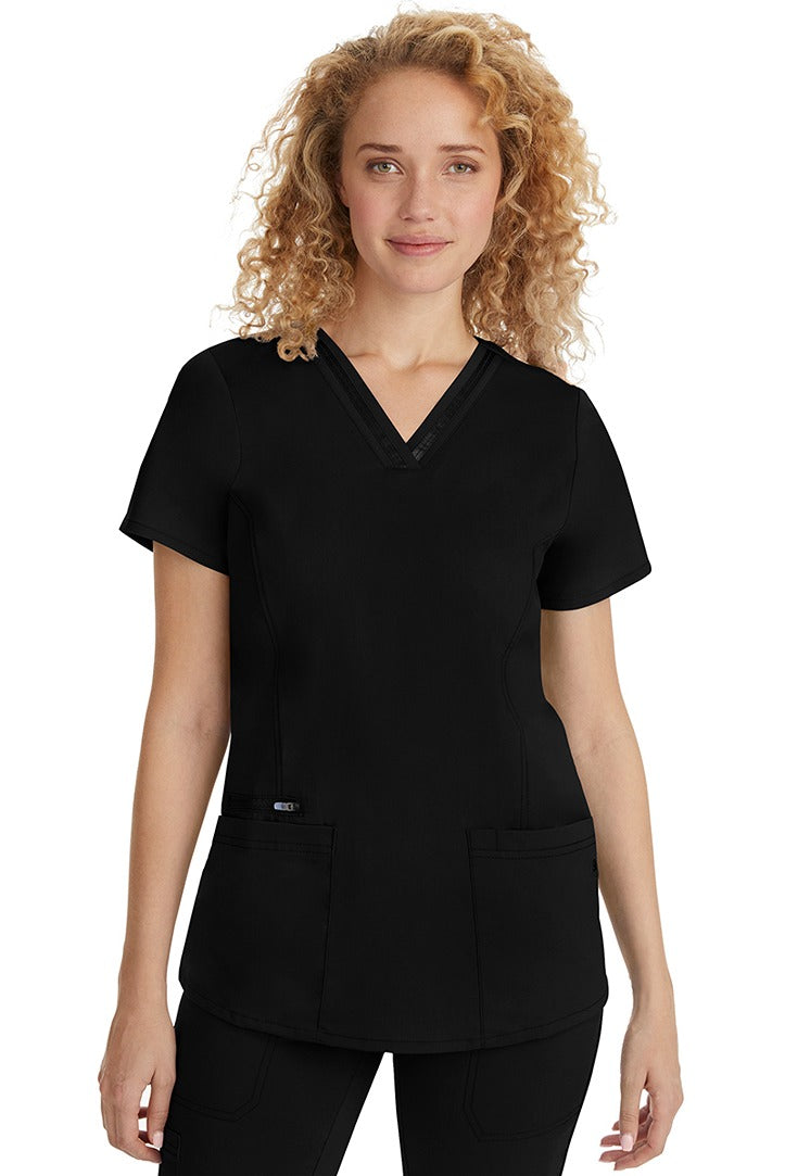 A female Nurse Practitioner wearing a Purple Label Women's Jasmin Fashion Scrub Top in Black featuring a trimmed v-neckline.