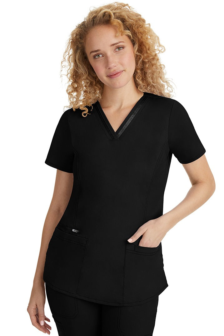 A female LPN wearing a Women's Jasmin Fashion V-Neck Scrub Top from Purple Label in Black featuring side vents at the hem for additional range of motion & to ensure a comfortable all day fit.