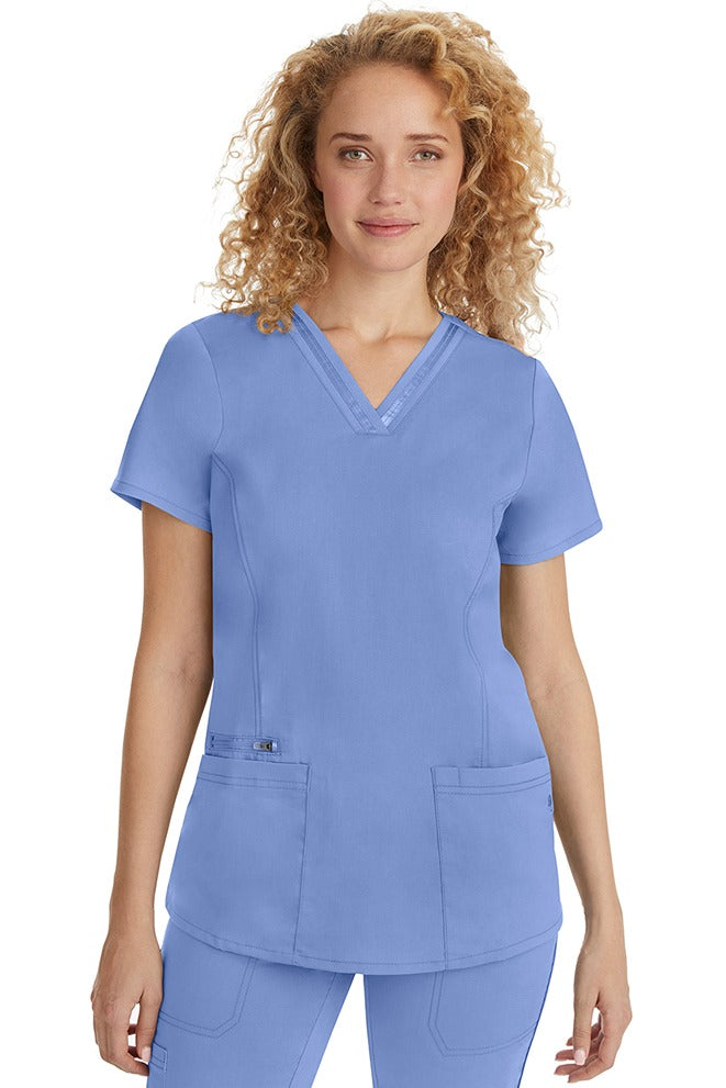A female Nurse Practitioner wearing a Purple Label Women's Jasmin Fashion Scrub Top in Ceil featuring a trimmed v-neckline.