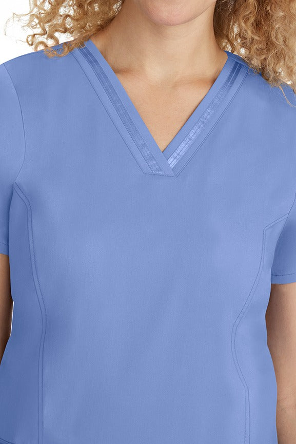 A young lady CNA wearing a Purple Label Women's Jasmin Fashion V-neck Scrub Top in Ceil featuring a super comfortable stretch fabric made of 96% polyester & 6% spandex.