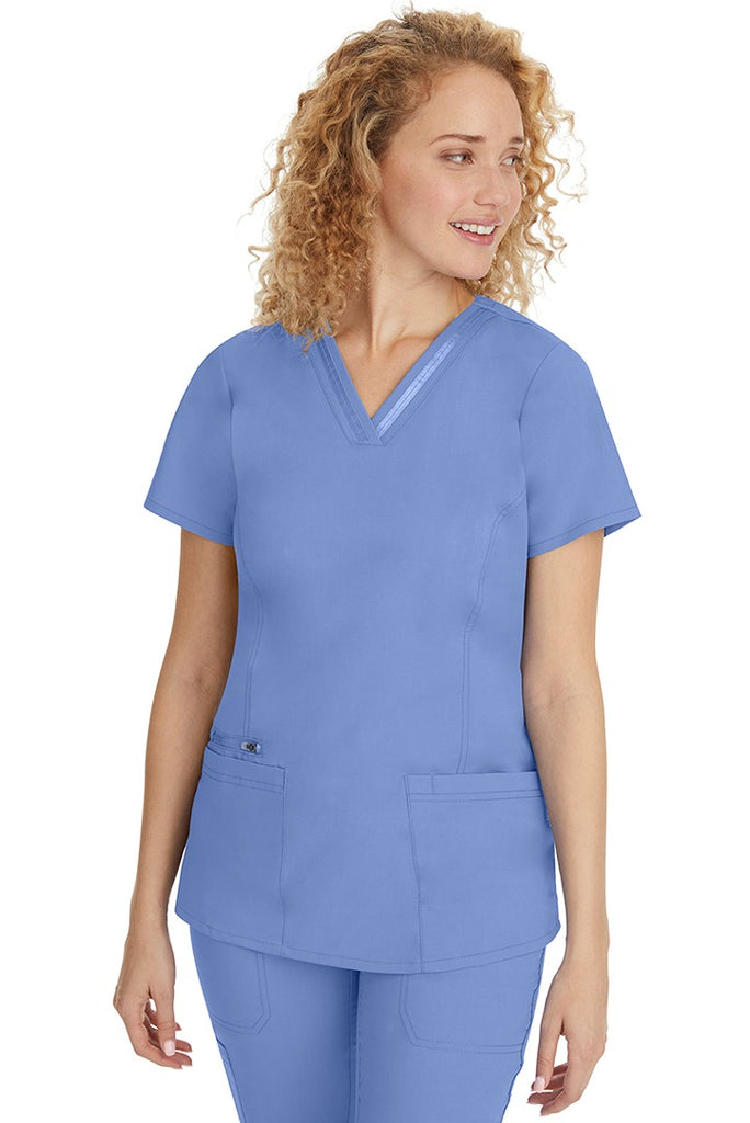 A young Home Care Registered Nurse wearing a Purple Label Women's Jasmin Fashion V-Neck Scrub Top in Ceil featuring front & back princess seams to provide a flattering fit.