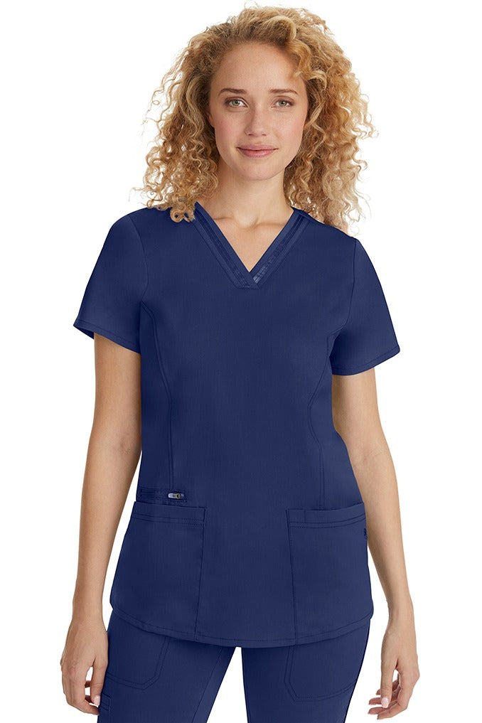 A female Nurse Practitioner wearing a Purple Label Women's Jasmin Fashion Scrub Top in Navy featuring a trimmed v-neckline.