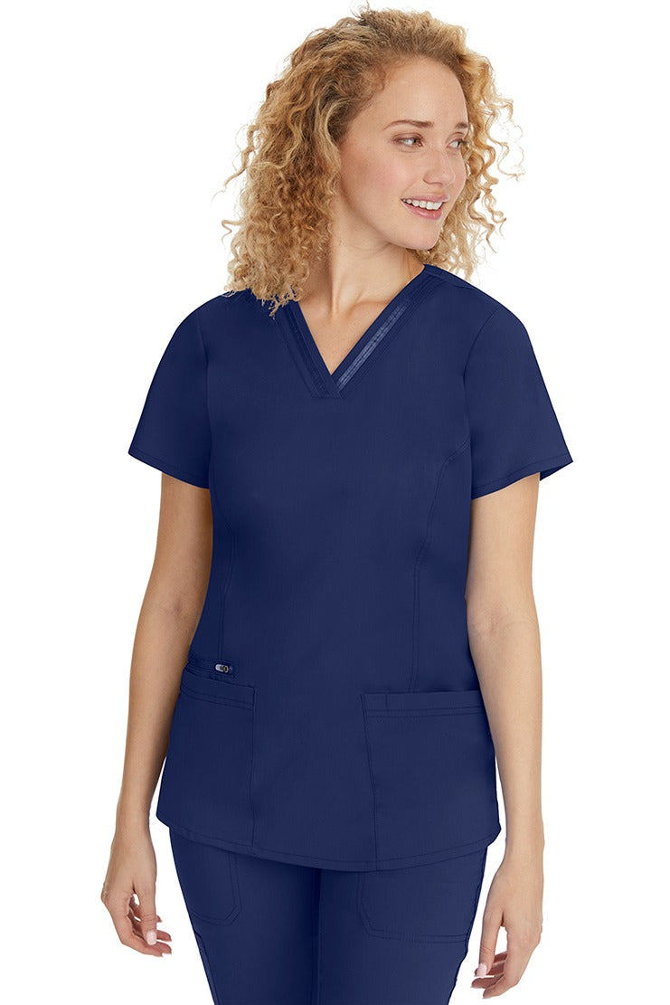 A young Home Care Registered Nurse wearing a Purple Label Women's Jasmin Fashion V-Neck Scrub Top in Navy featuring front & back princess seams to provide a flattering fit.
