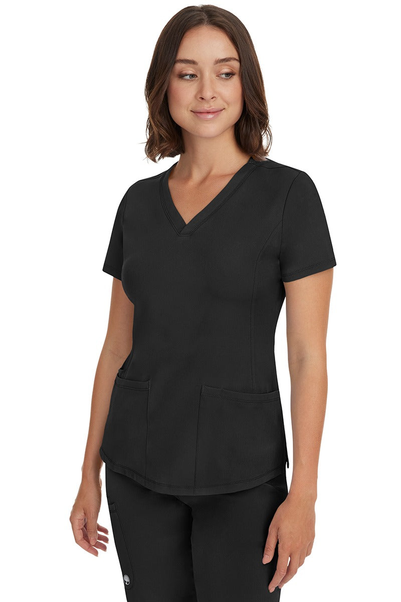 A young female healthcare professional wearing a HH-Works Women's Monica Multi-Pocket Scrub Top in Black featuring a center back length of 24".