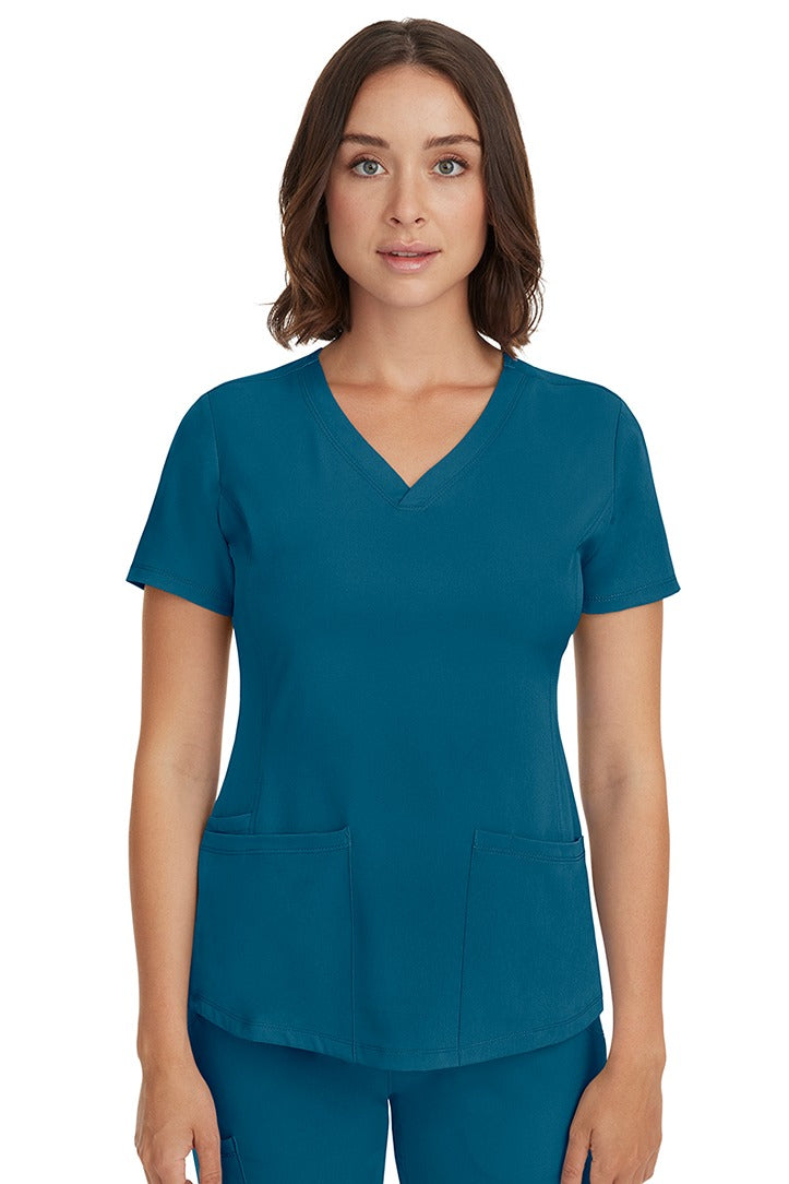 A young female LPN wearing a HH-Works Women's Monica Multi-Pocket Scrub Top in Caribbean featuring short sleeves & a v-neckline.