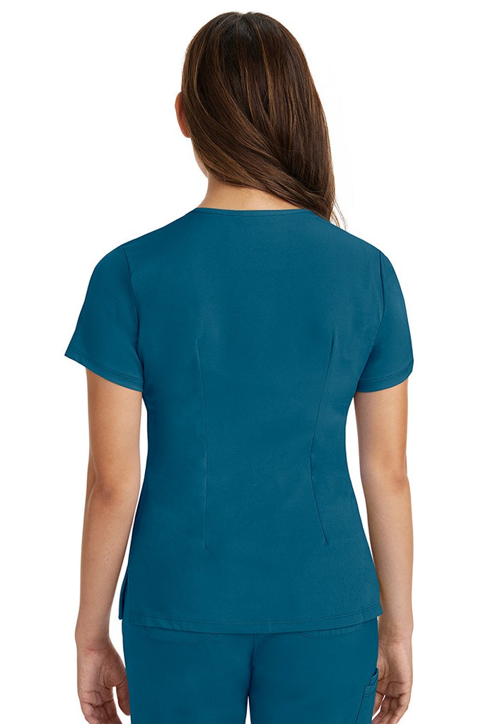 A female registered nurse wearing a Women's Monica Multi-Pocket Scrub Top from HH Works in Caribbean featuring back princess darts for shaping.