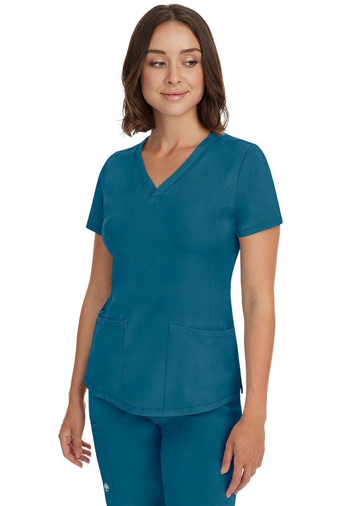 A young female healthcare professional wearing a HH-Works Women's Monica Multi-Pocket Scrub Top in Caribbean featuring a center back length of 24".