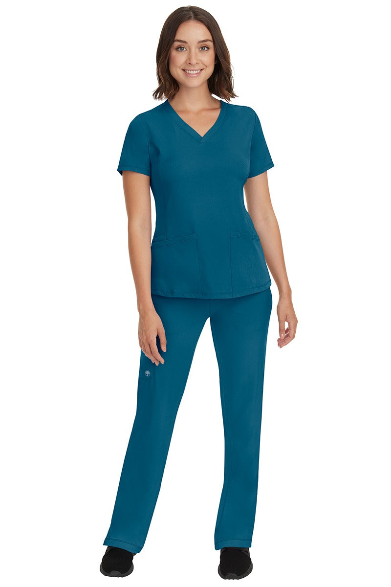 A young female nurse wearing a Women's Monica Multi-Pocket Scrub Top from HH Works in Caribbean featuring unique stretch fabric made of 91% polyester & 9% spandex.