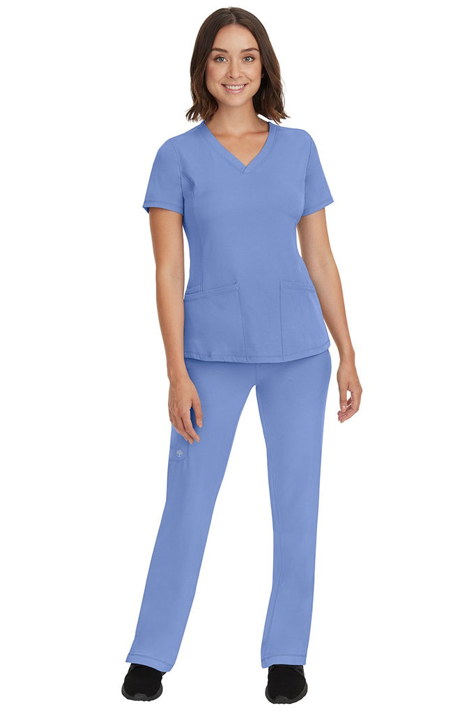 A young female nurse wearing a Women's Monica Multi-Pocket Scrub Top from HH Works in Ceil featuring unique stretch fabric made of 91% polyester & 9% spandex.