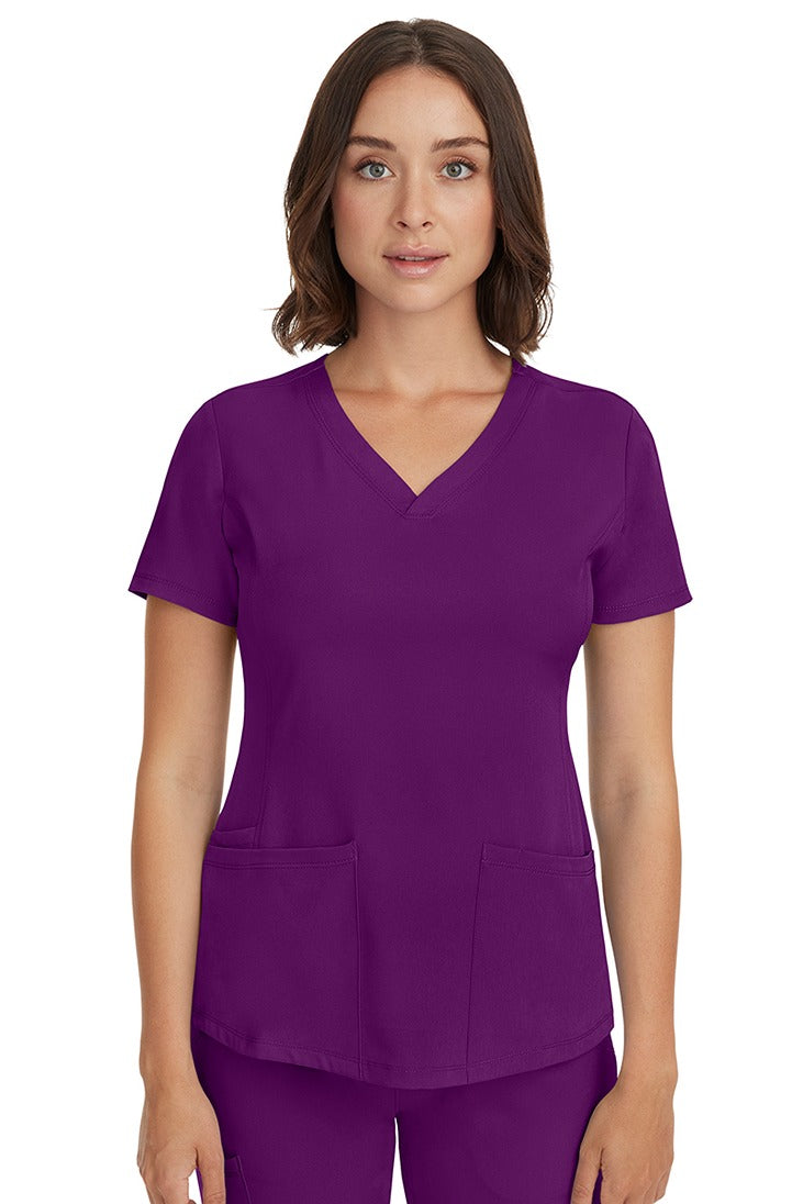 A young female LPN wearing a HH-Works Women's Monica Multi-Pocket Scrub Top in Eggplant featuring short sleeves & a v-neckline.