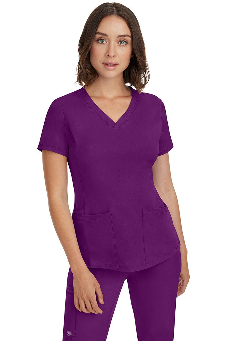 A female Nurse Practitioner wearing an HH-Works Women's Monica Multi-Pocket Scrub Top in Eggplant featuring a total of 4 pockets.