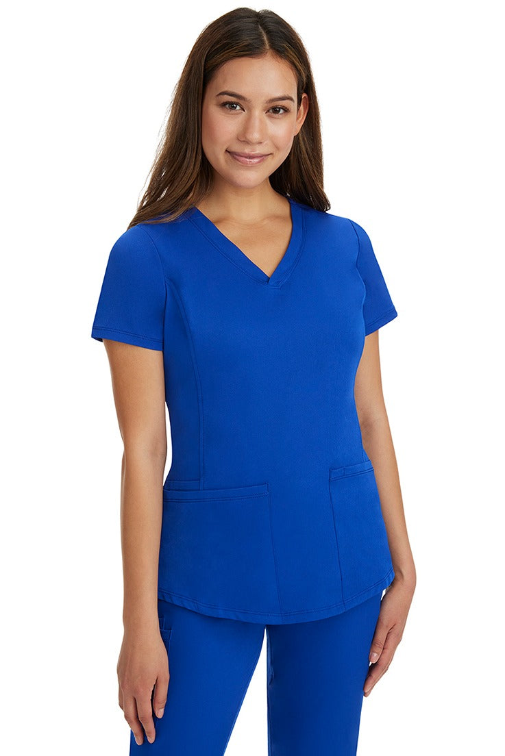 A young female healthcare professional wearing a HH-Works Women's Monica Multi-Pocket Scrub Top in Galaxy Blue featuring a center back length of 24".