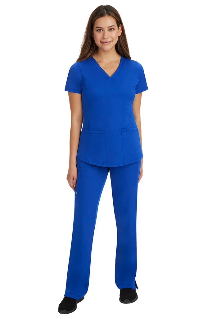 A young female nurse wearing a Women's Monica Multi-Pocket Scrub Top from HH Works in Galaxy Blue featuring unique stretch fabric made of 91% polyester & 9% spandex.