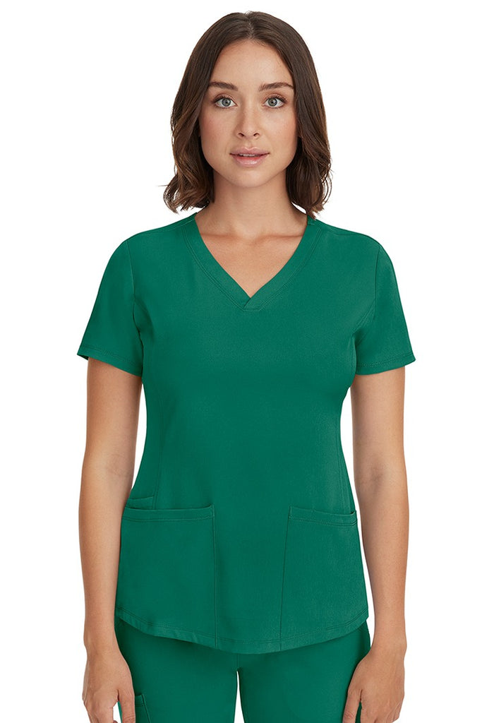 A young female LPN wearing a HH-Works Women's Monica Multi-Pocket Scrub Top in Hunter Green featuring short sleeves & a v-neckline.
