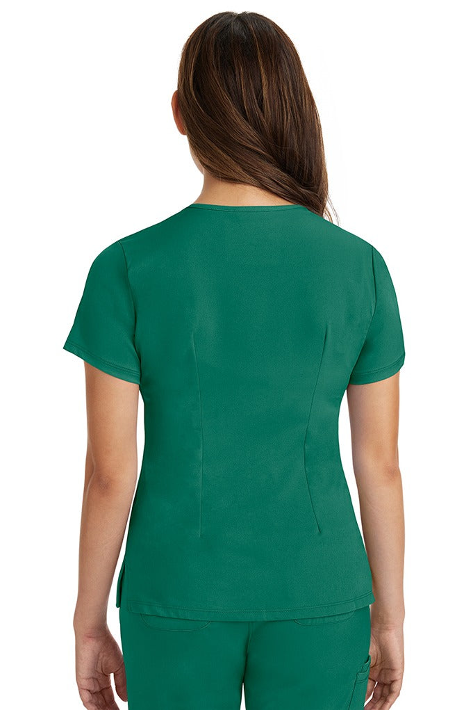A female registered nurse wearing a Women's Monica Multi-Pocket Scrub Top from HH Works in Hunter Green featuring back princess darts for shaping.