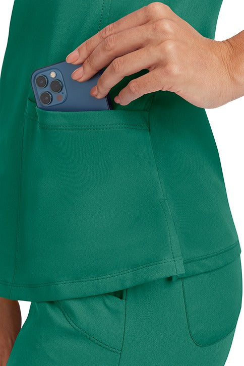 A young Home Care Registered Nurse wearing a HH-Works Women's Monica Multi-Pocket Scrub Top in Hunter featuring side slits for additional range of motion.