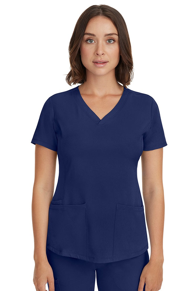 A young female LPN wearing a HH-Works Women's Monica Multi-Pocket Scrub Top in Navy featuring short sleeves & a v-neckline.