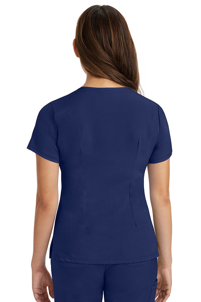 A female registered nurse wearing a Women's Monica Multi-Pocket Scrub Top from HH Works in Navy featuring back princess darts for shaping.