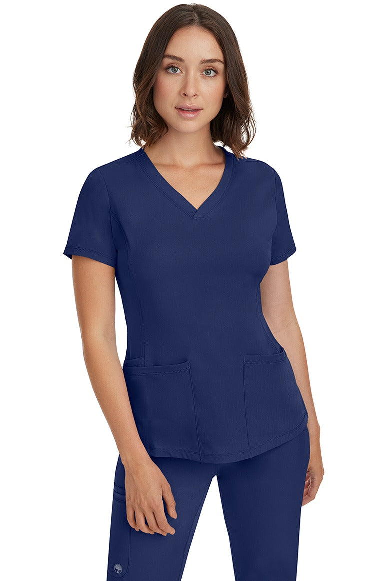 A female Nurse Practitioner wearing an HH-Works Women's Monica Multi-Pocket Scrub Top in Navy featuring a total of 4 pockets.