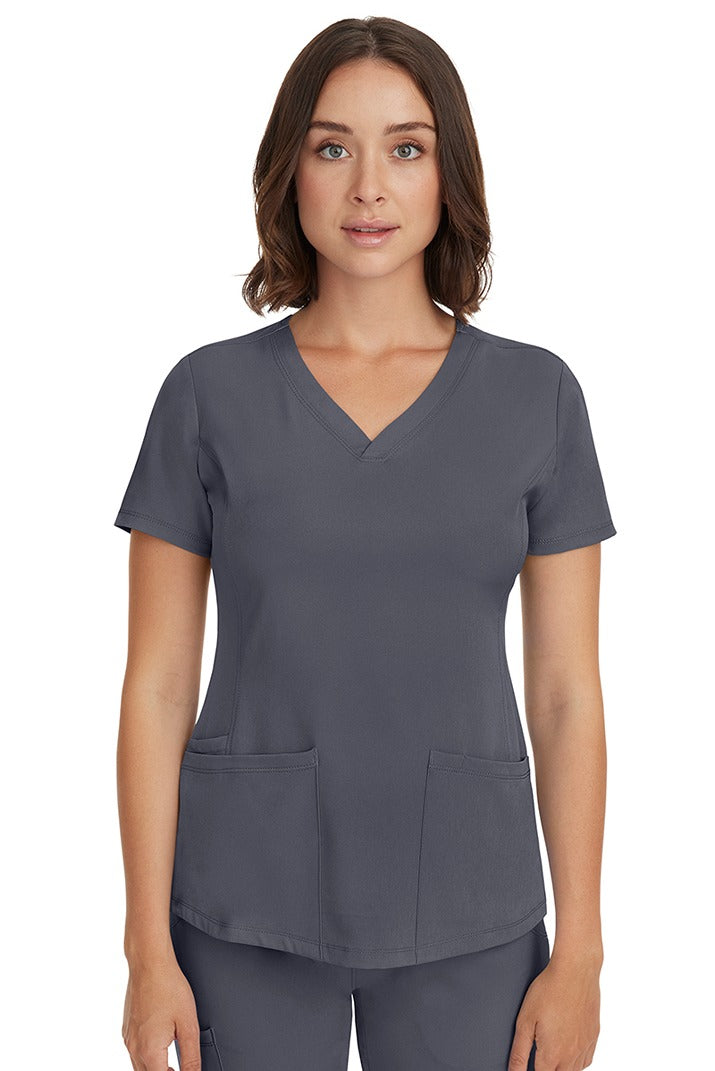 A young female LPN wearing a HH-Works Women's Monica Multi-Pocket Scrub Top in Pewter featuring short sleeves & a v-neckline.