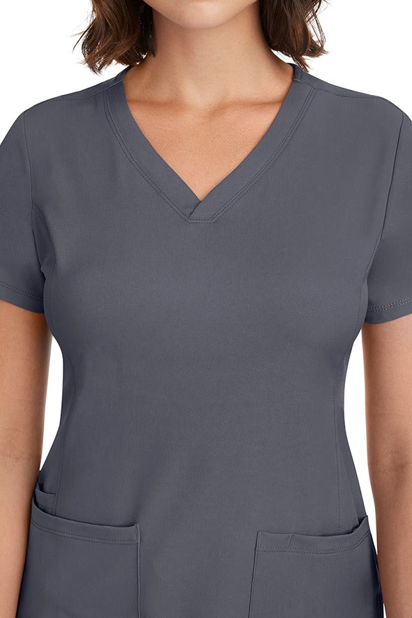 A young woman CNA wearing a HH-Works Women's Monica Multi-Pocket Scrub Top in Pewter featuring front princess seaming to ensure a flattering fit.