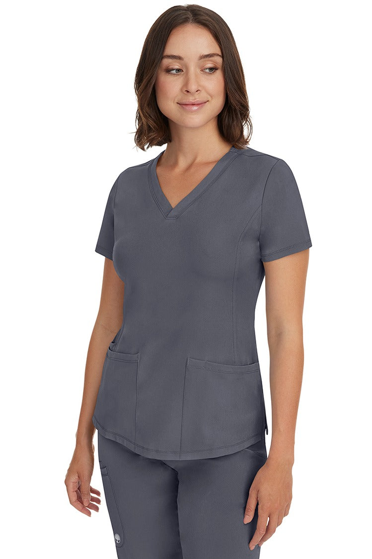 A young female healthcare professional wearing a HH-Works Women's Monica Multi-Pocket Scrub Top in Pewter featuring a center back length of 24".