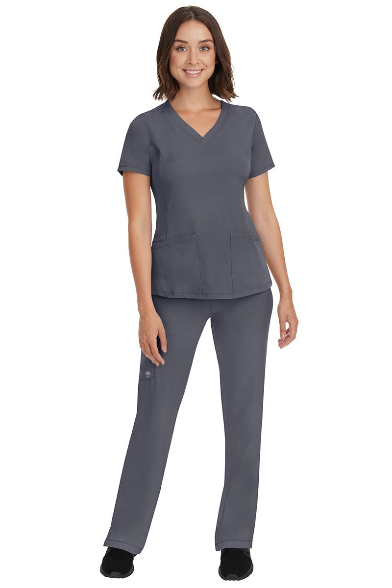 A young female nurse wearing a Women's Monica Multi-Pocket Scrub Top from HH Works in Pewter featuring unique stretch fabric made of 91% polyester & 9% spandex.