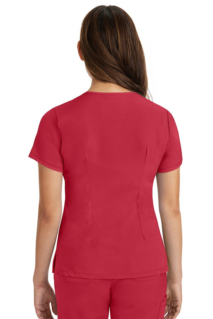 A female registered nurse wearing a Women's Monica Multi-Pocket Scrub Top from HH Works in Red featuring back princess darts for shaping.