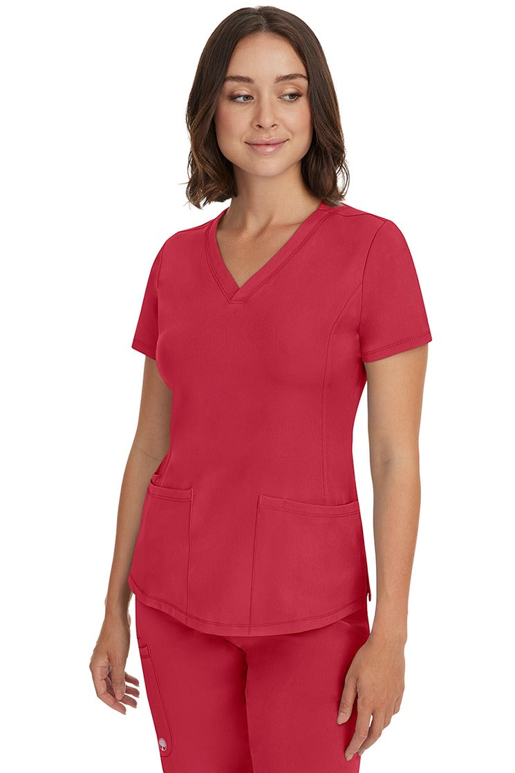 A young female healthcare professional wearing a HH-Works Women's Monica Multi-Pocket Scrub Top in Red featuring a center back length of 24".