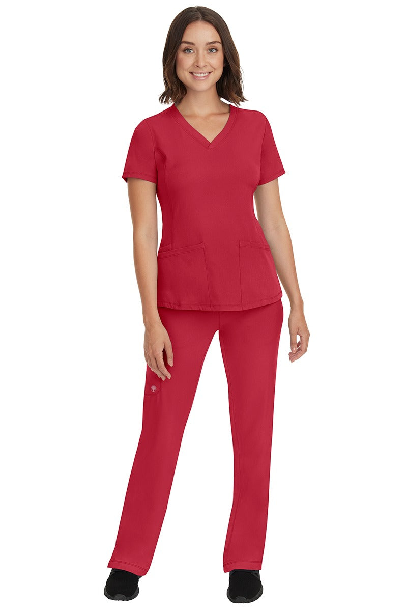 A young female nurse wearing a Women's Monica Multi-Pocket Scrub Top from HH Works in Red featuring unique stretch fabric made of 91% polyester & 9% spandex.