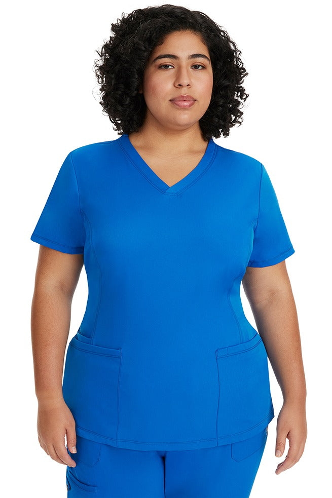 A young female LPN wearing a HH-Works Women's Monica Multi-Pocket Scrub Top in Royal featuring short sleeves & a v-neckline.