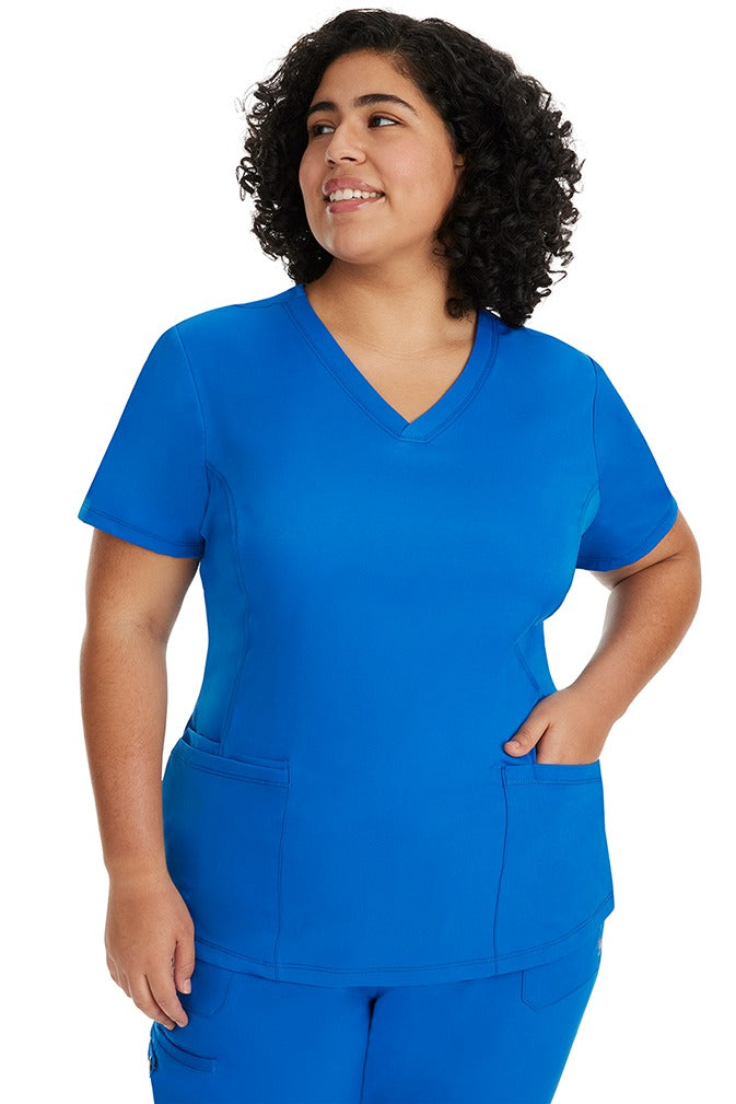 A young Home Care Registered Nurse wearing a HH-Works Women's Monica Multi-Pocket Scrub Top in Royal featuring side slits for additional range of motion.