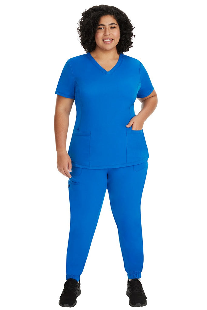 A young female nurse wearing a Women's Monica Multi-Pocket Scrub Top from HH Works in Black featuring unique stretch fabric made of 91% polyester & 9% spandex.