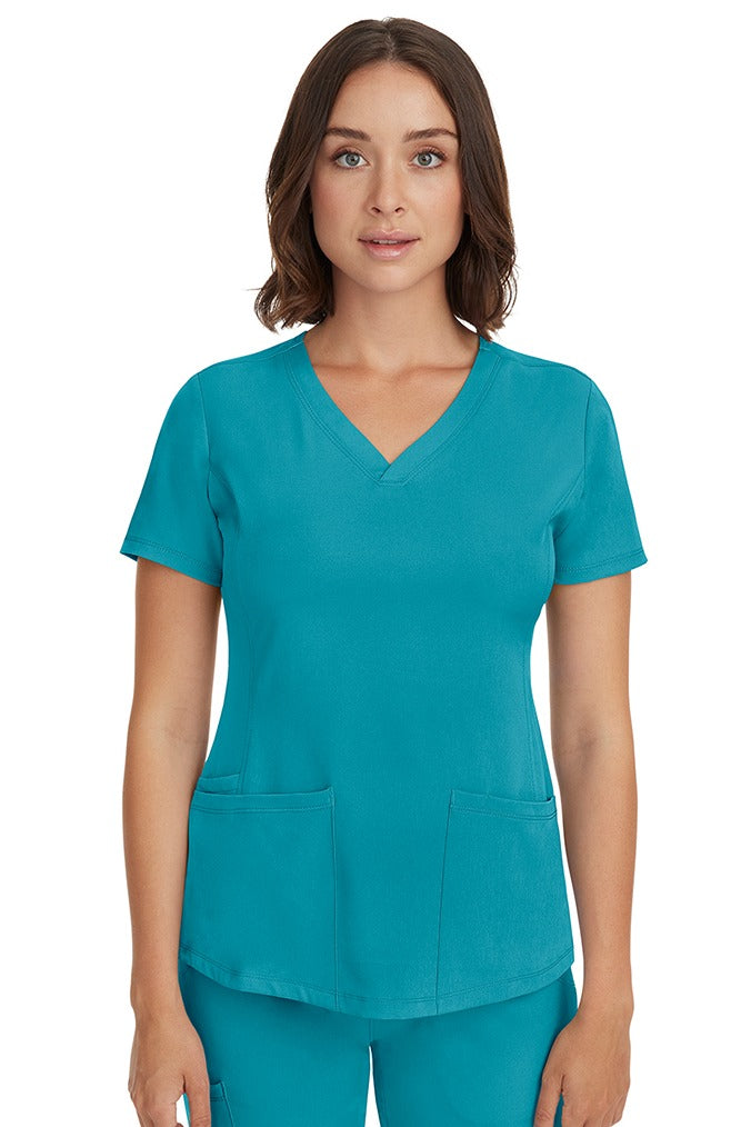 A young female LPN wearing a HH-Works Women's Monica Multi-Pocket Scrub Top in Teal featuring short sleeves & a v-neckline.