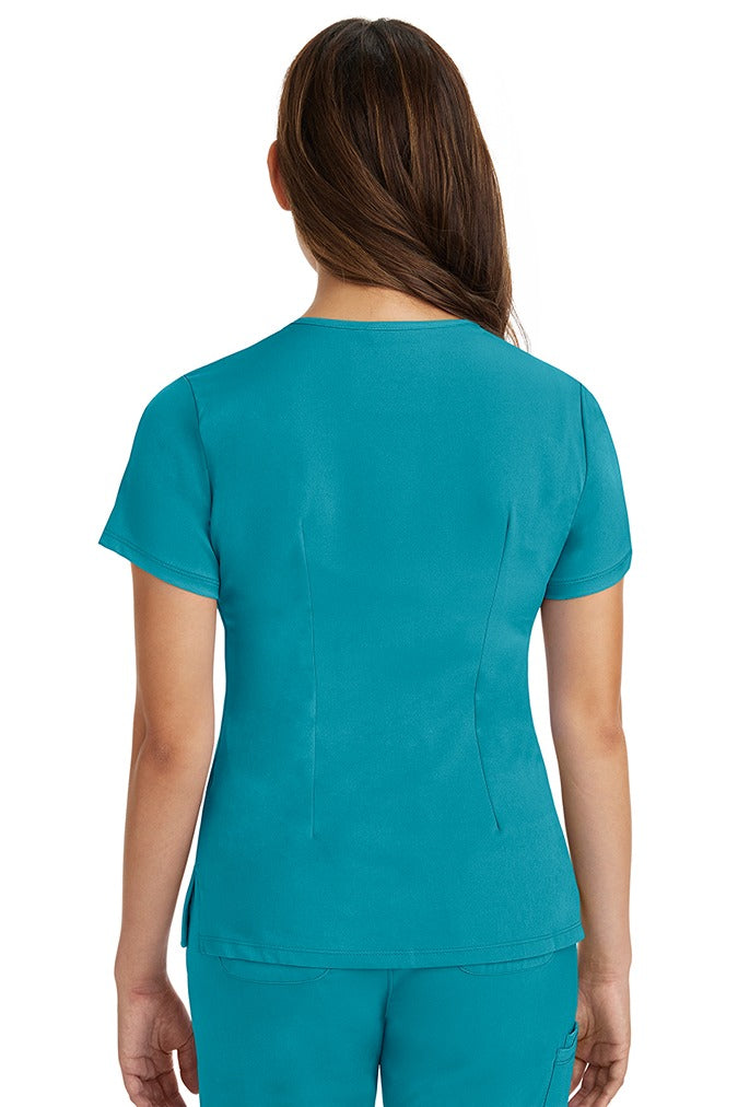A female registered nurse wearing a Women's Monica Multi-Pocket Scrub Top from HH Works in Teal featuring back princess darts for shaping.