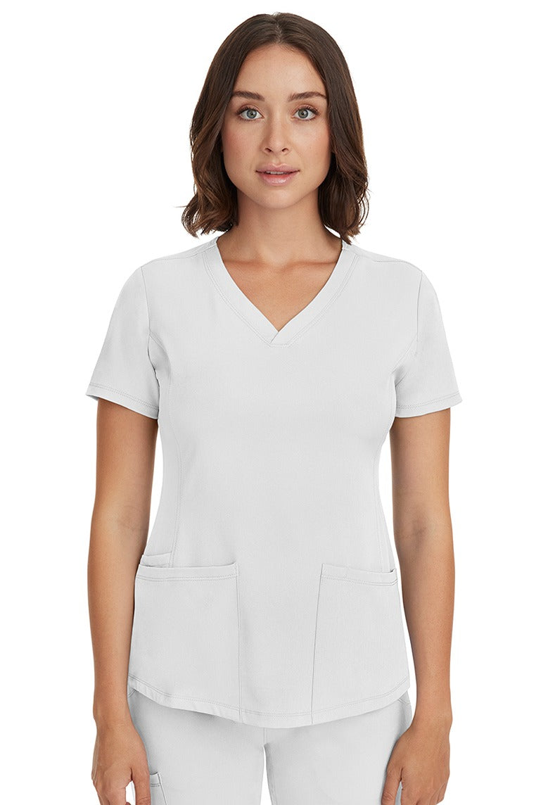 A young female LPN wearing a HH-Works Women's Monica Multi-Pocket Scrub Top in White featuring short sleeves & a v-neckline.