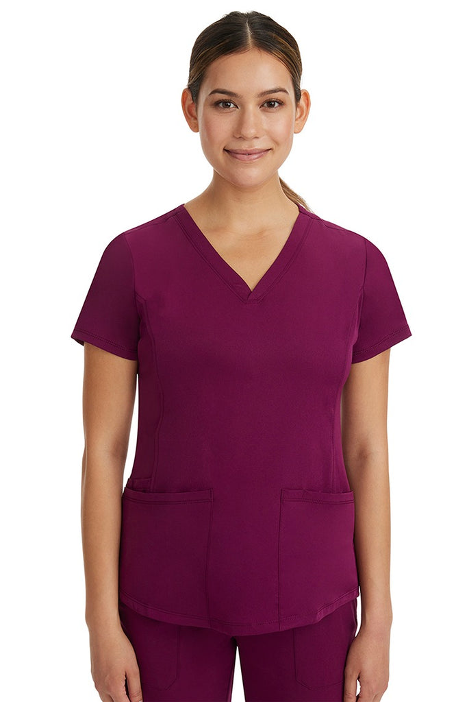 A young female Cardiovascular Nurse wearing a HH-Works Women's Monica Multi-Pocket Scrub Top in Wine featuring short sleeves & a v-neckline.
