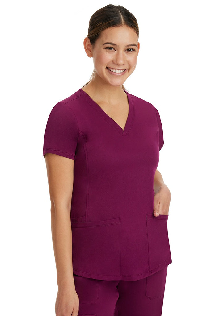 A young Home Care Registered Nurse wearing a HH-Works Women's Monica Multi-Pocket Scrub Top in Wine featuring side slits for additional range of motion.