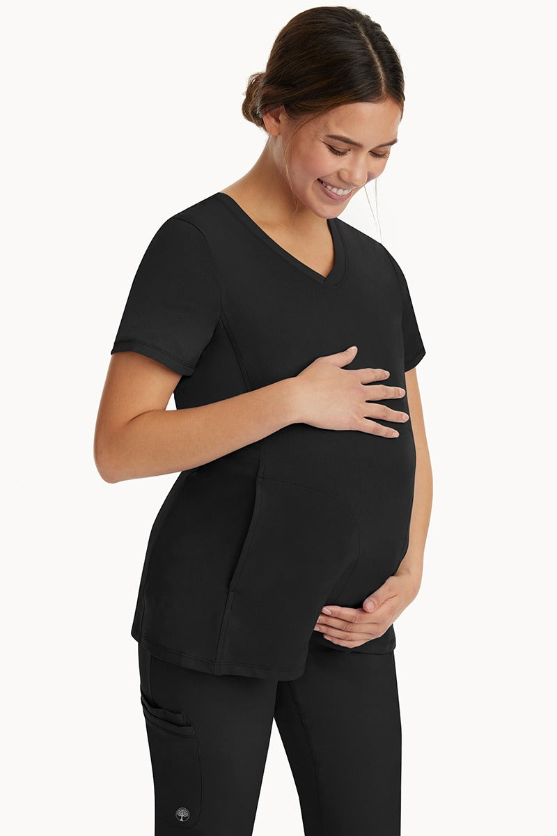 A young woman wearing an HH-Works Women's Mila Maternity V-Neck Scrub Top in Black featuring adjustable side panels. 