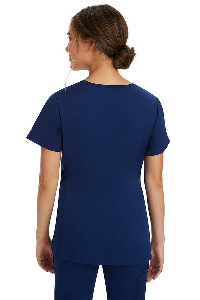 A young lady CNA wearing a Women's Mila Maternity V-Neck Scrub Top from HH Works in Navy featuring a shaping bungee chord to ensure a flattering fit.