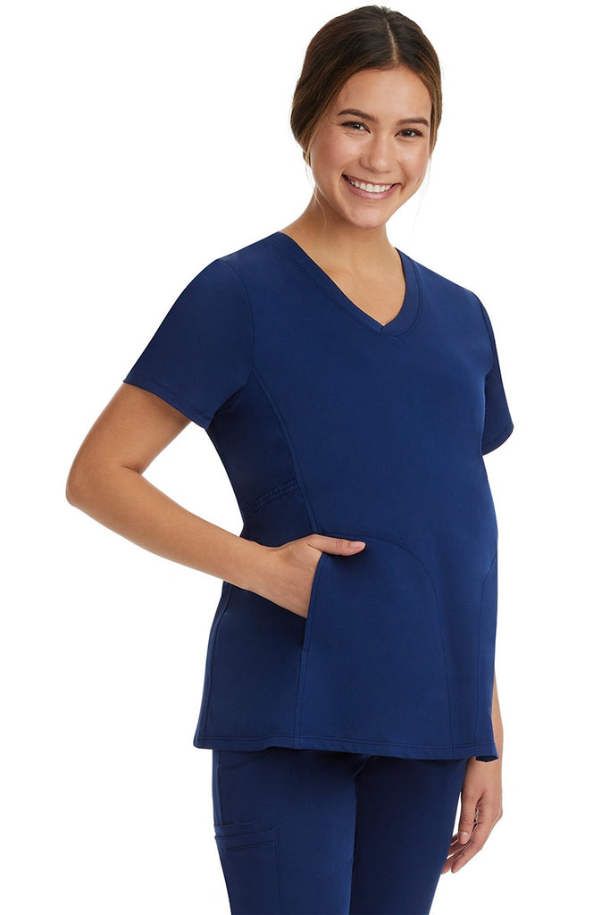 A young woman wearing an HH-Works Women's Mila Maternity V-Neck Scrub Top in Navy featuring adjustable side panels.