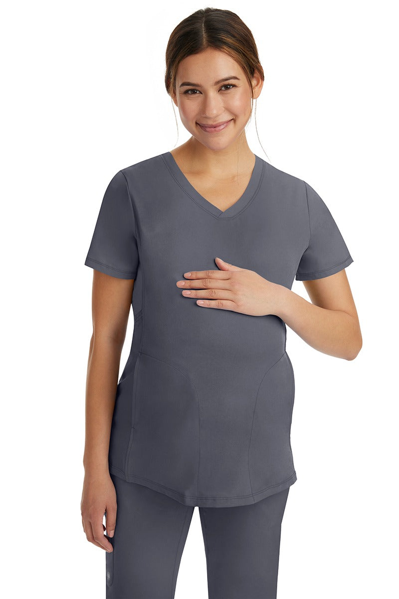 A pregnant female LPN wearing an HH-Works Women's Mila Maternity V-Neck Scrub Top in Pewter featuring a v-neckline & short sleeves.