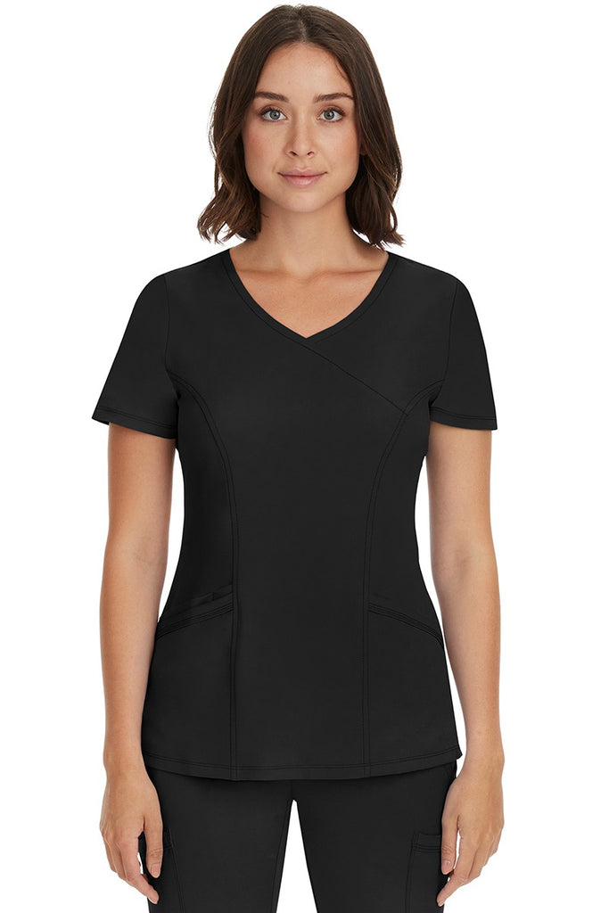 A young female Registered Nurse wearing an  HH-Works Women's Madison Mock Wrap Scrub Top in Black featuring a faux wrap neckline.