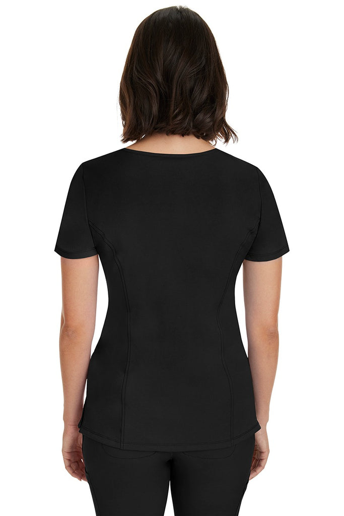 A young woman wearing a HH-Works Women's Madison Mock Wrap Scrub Top in Black featuring princess seams throughout.