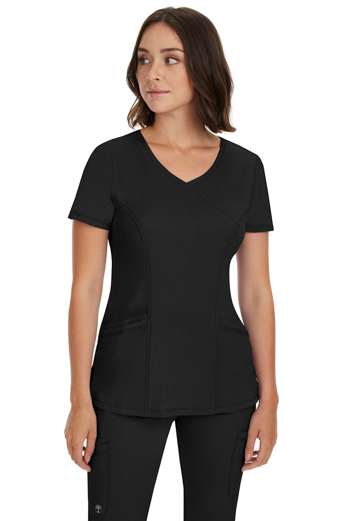 A young Home Care Registered Nurse wearing a HH-Works Women's Madison Mock Wrap Scrub Top in Black featuring a total of 4 pockets for all of your on the go storage needs.